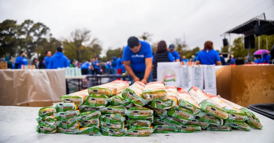 Food parcels stacked on a distribution table, volunteers in the background.