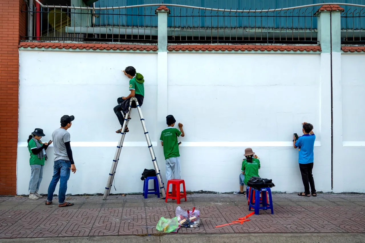 Group of young people preparing a mural along a long white wall, one of them on a stepladder.