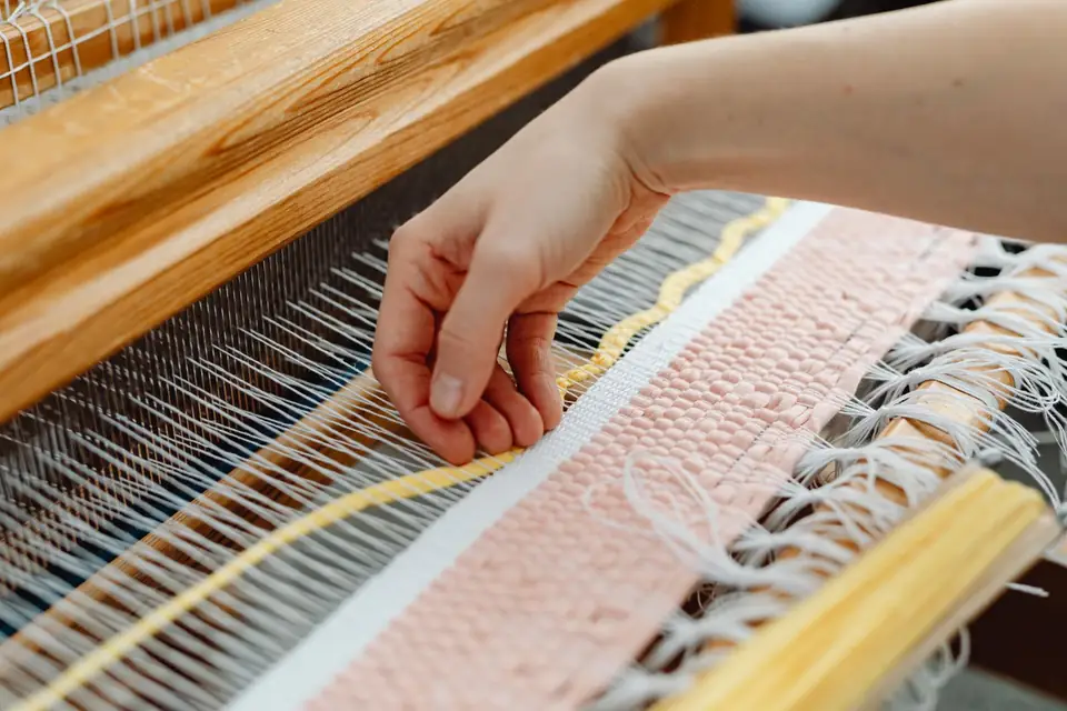 Hand weaving threads on a wooden loom.