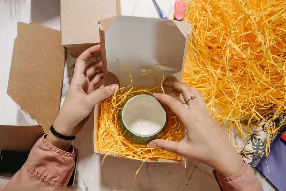 Hands placing a ceramic bowl in a box filled with shredded paper.