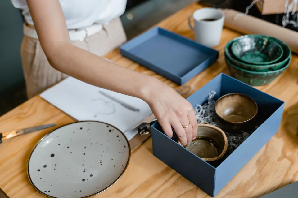Maker packing ceramic bowls into a blue box, with a speckled plate beside it.