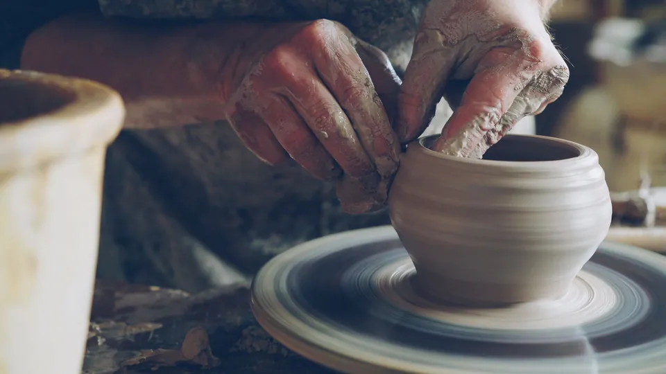 Hands shaping a clay pot on a potter’s wheel.