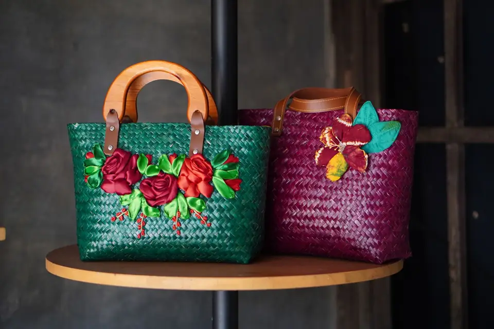 Two handwoven bags embroidered with flowers on a display stand.