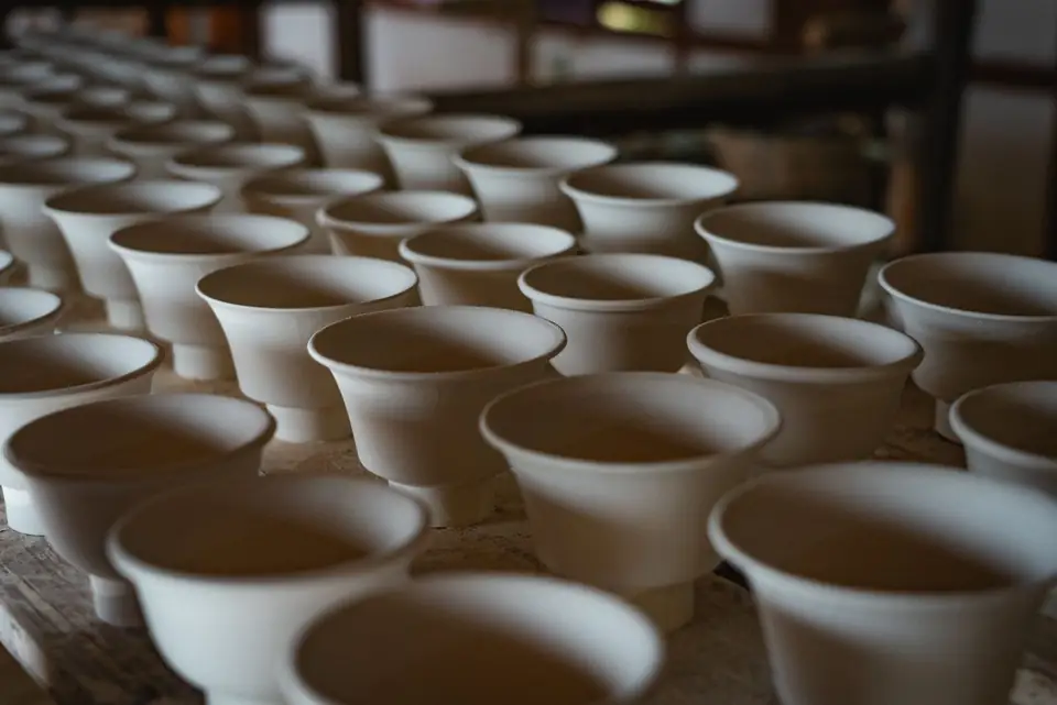 Batch of white ceramic cups lined up on a workshop table.