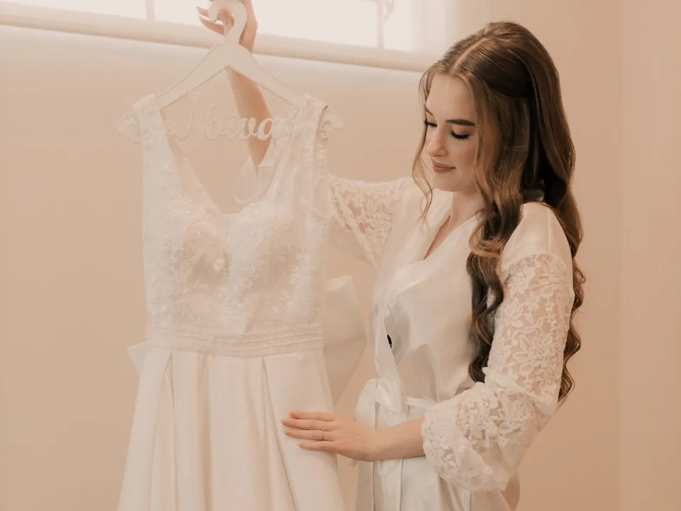 Bride-to-be adjusting her white gown hanging by a window.