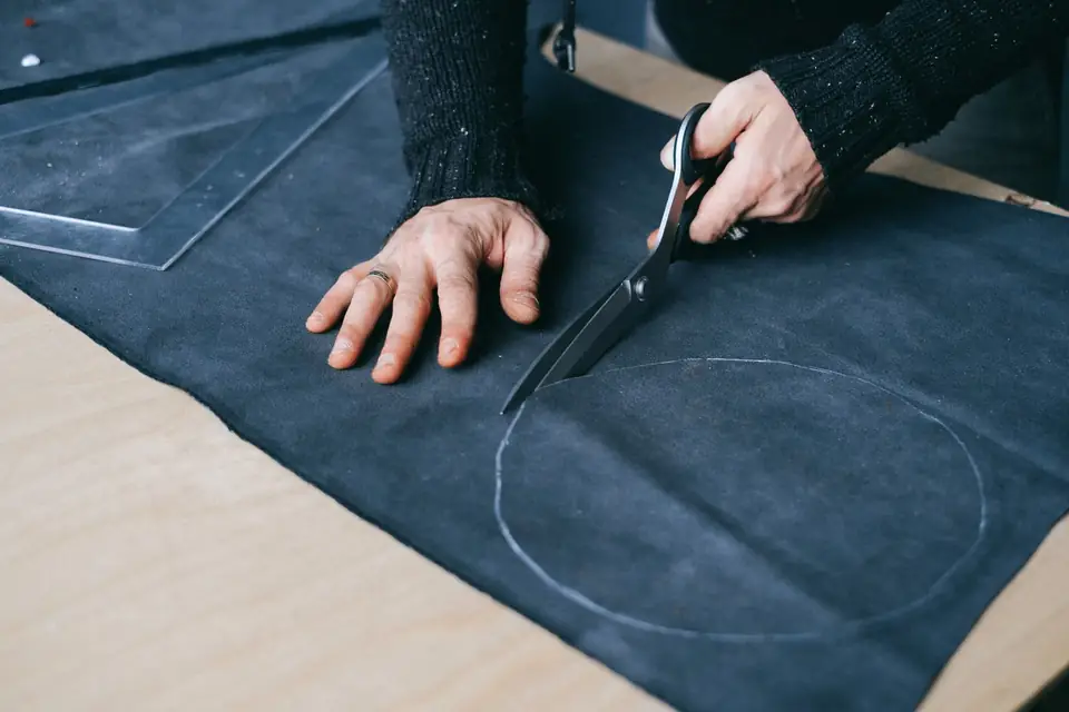 Tailor cutting a chalk-marked piece of fabric with scissors.