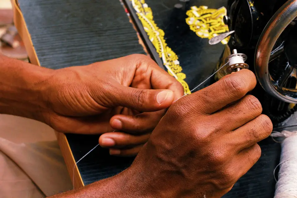 Hands threading the needle of a vintage sewing machine.