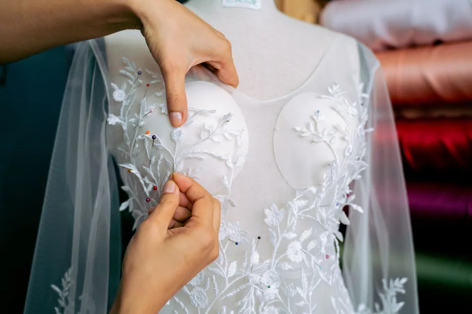 Hands adjusting a tulle dress embroidered with white flowers on a dress form.