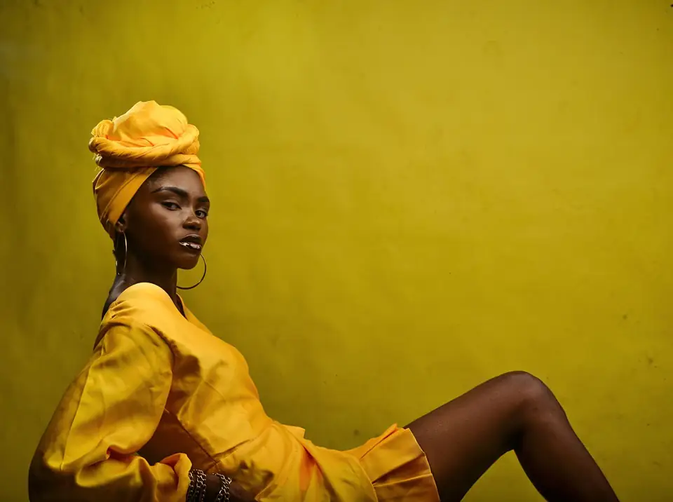 Woman in a yellow dress and head wrap posing against a yellow background.