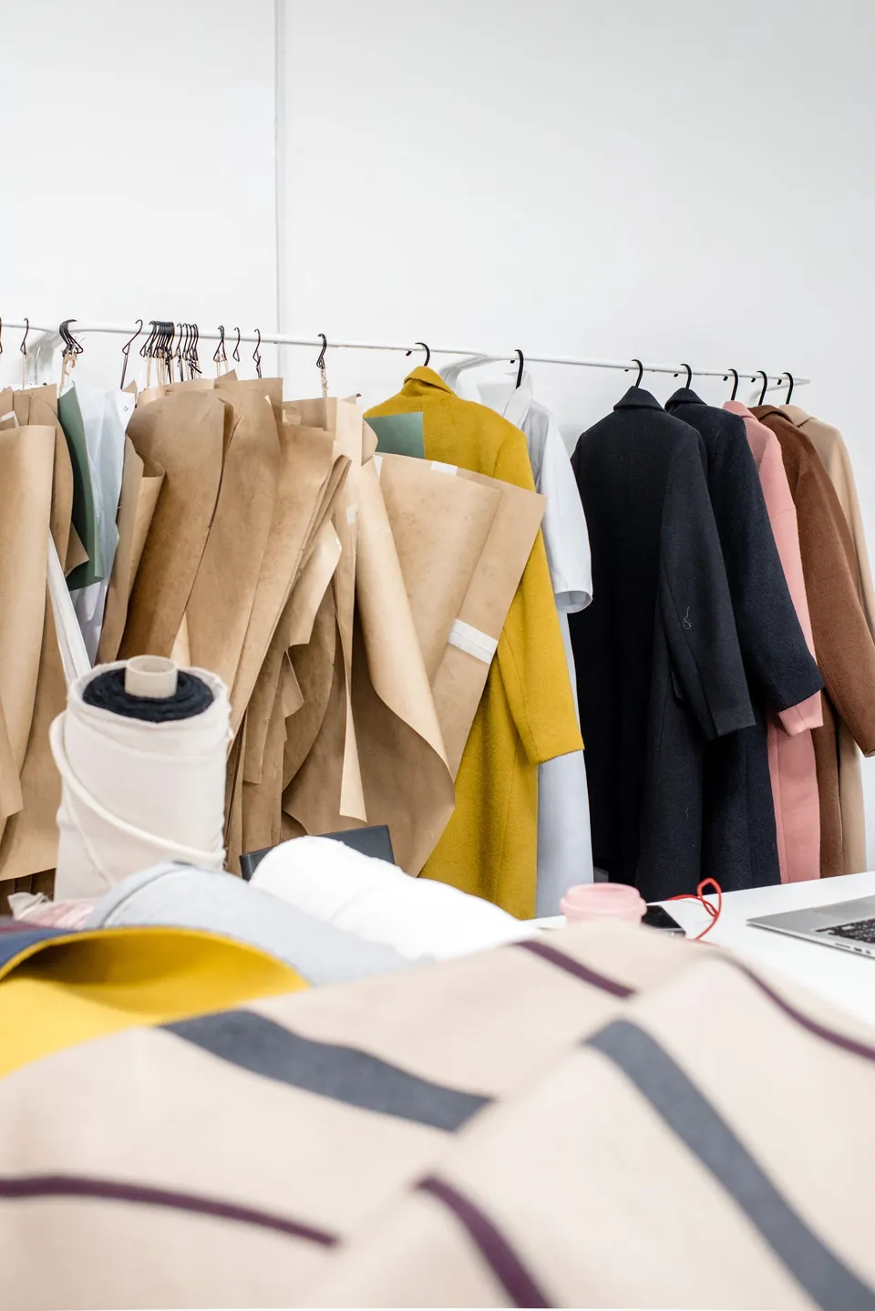 Clothing rack and hanging patterns behind fabric rolls in a fashion workshop.