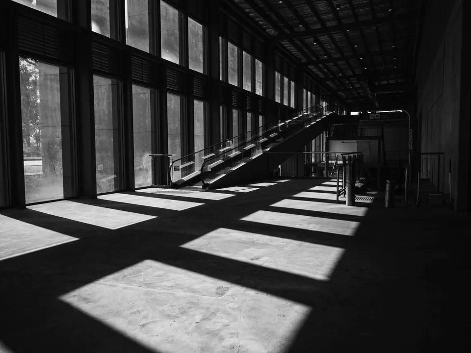 Dark hall where tall windows cast rectangles of light on the floor, black and white.