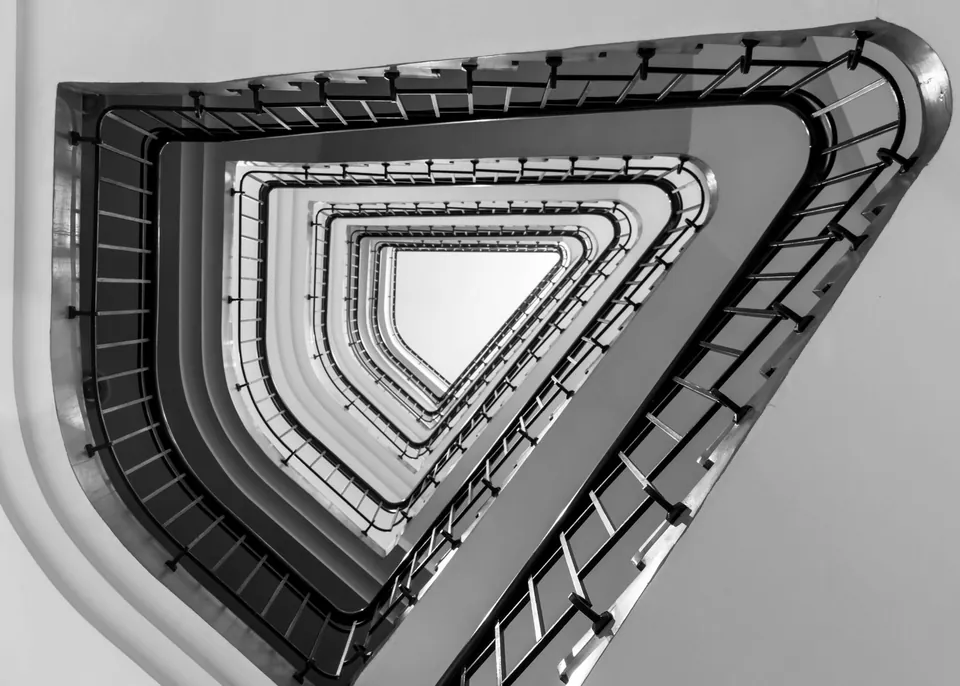 Triangular stairwell seen from below, a spiral of railings, black and white.