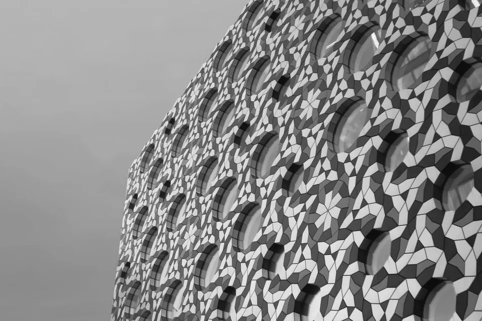 Geometric mosaic facade pierced with round windows against the sky, black and white.