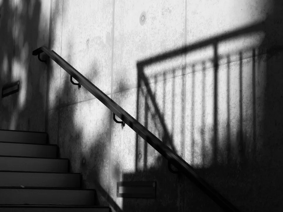 Shadow of a stair railing cast on a concrete wall, black and white.