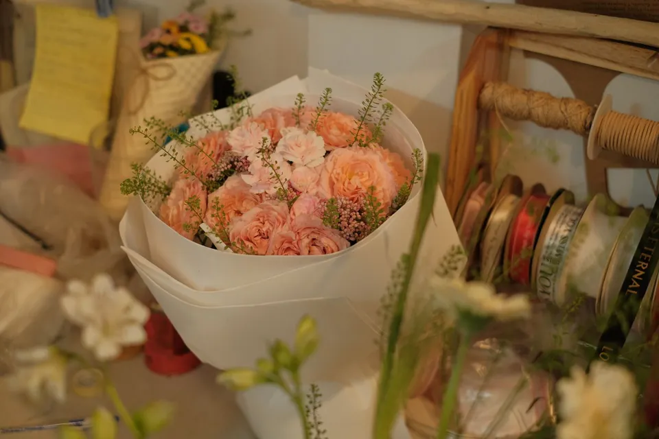 Bouquet of peach roses wrapped in white paper, next to ribbon spools.