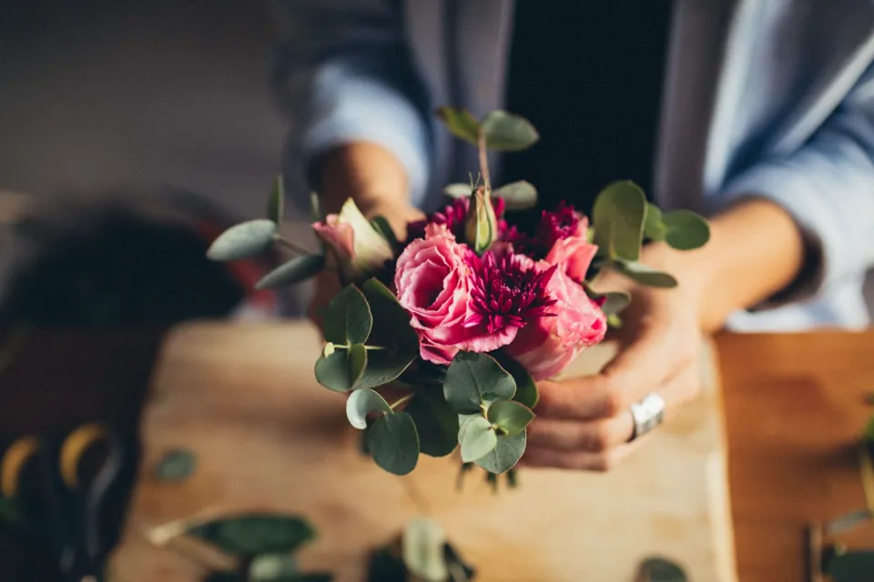 Hands presenting a small bouquet of fuchsia roses and eucalyptus.