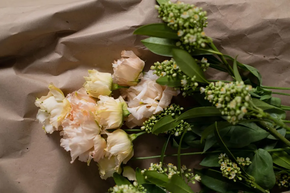 Cream roses and green flowers laid on kraft paper.