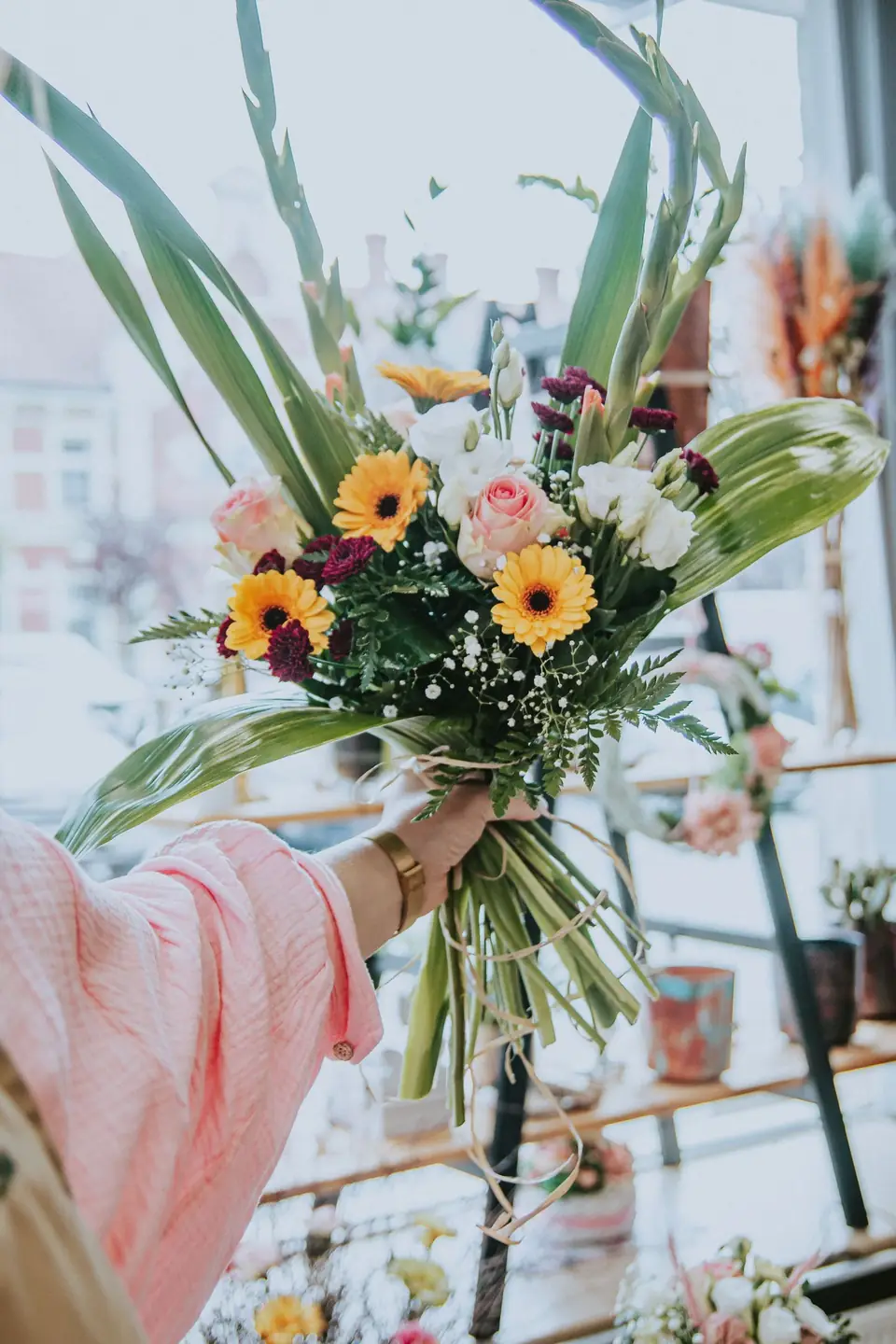 Bouquet of gerberas and foliage held at arm’s length in a flower shop.