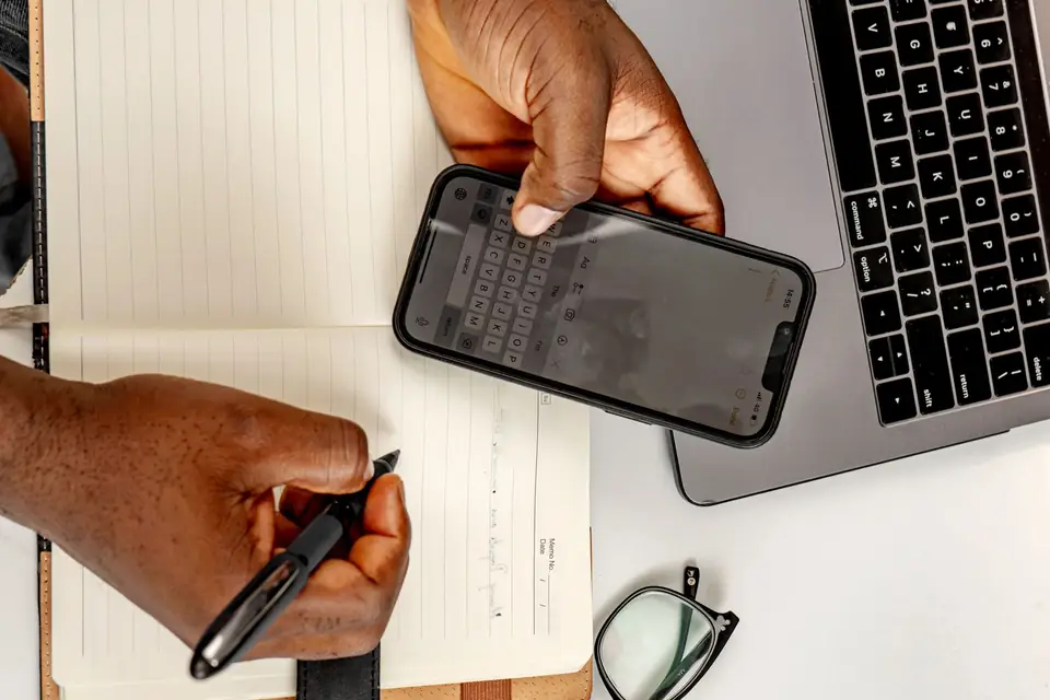 Hands writing a few lines in a notebook while holding a phone.