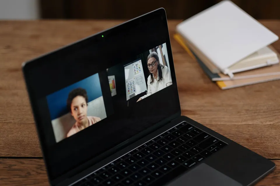Laptop open on a video call between two people, on a wooden table.