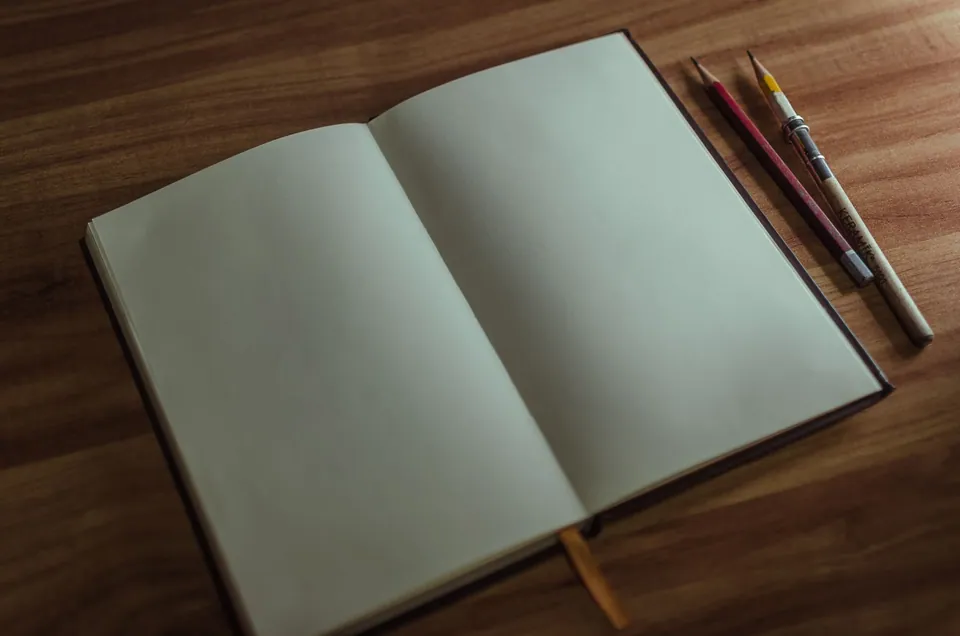 Open blank notebook and pencils on a wooden desk.
