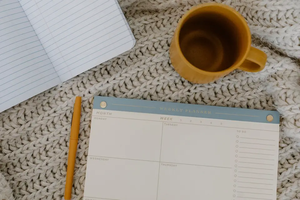 Weekly planner, notebook and mug on a knitted blanket.