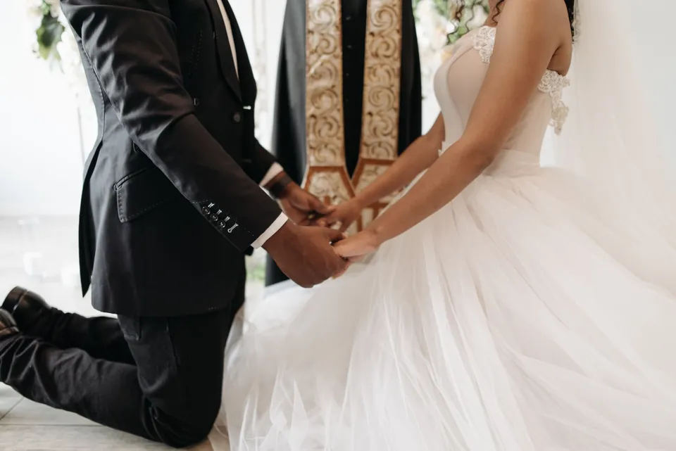 The groom, on one knee, holds the hands of the bride in a tulle gown.