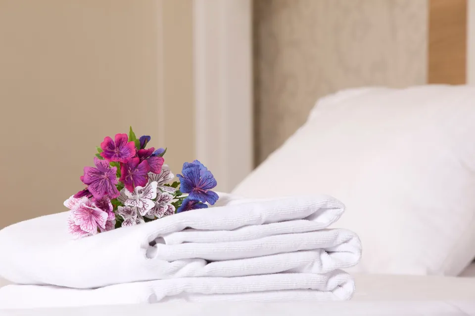 Folded towels and a small bouquet on a hotel bed.
