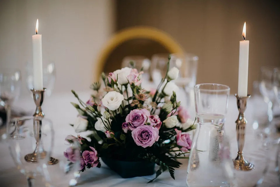 A festive table set with candles, glasses and a bouquet of mauve roses.