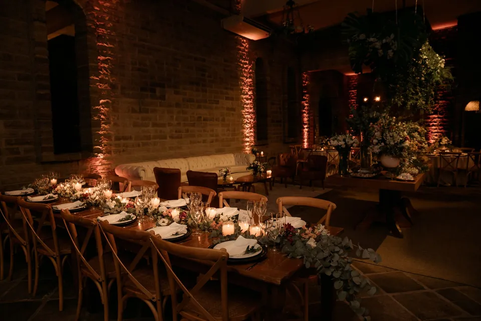 A long dinner table set in a brick-walled room under warm lighting.