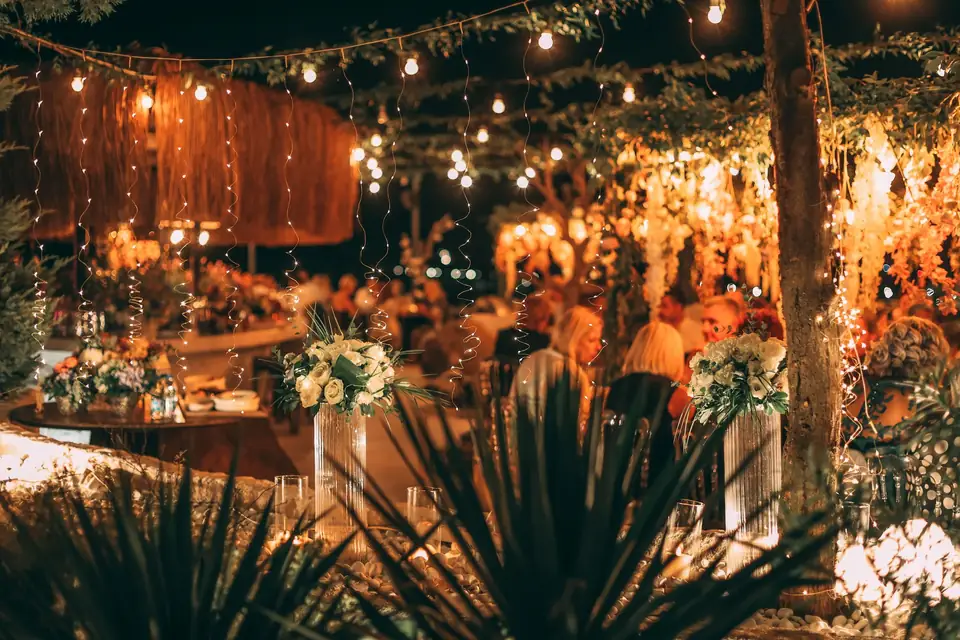 An outdoor evening reception with string lights and white bouquets on the tables.
