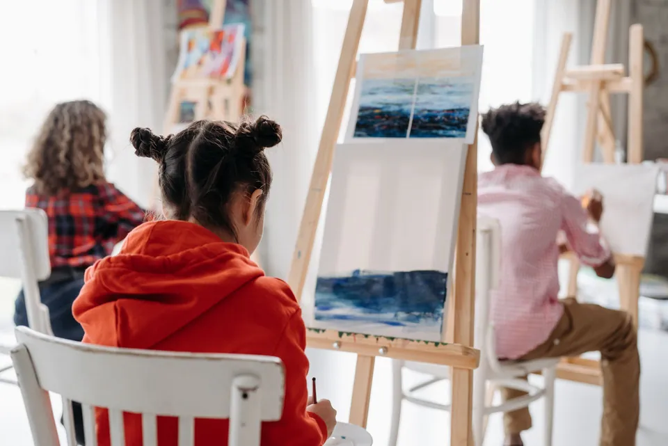 Pupils, seen from behind, painting at easels in an art studio.