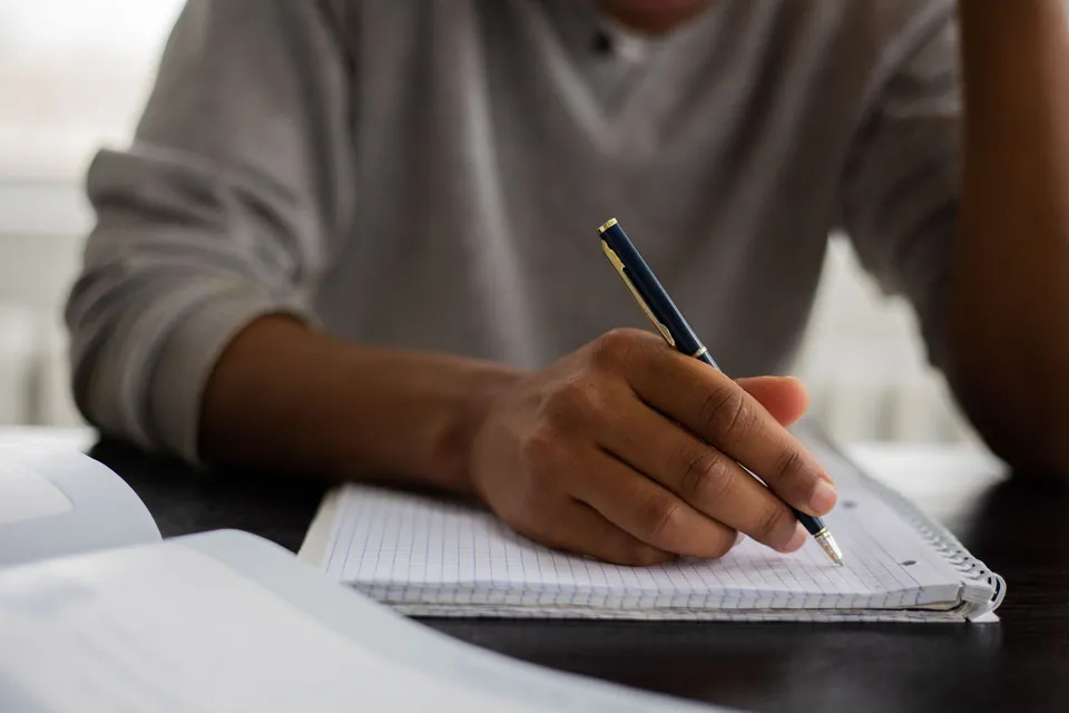 Hand taking notes with a pen in a spiral notebook.