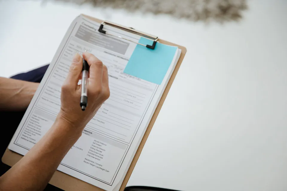 Hand filling in a form on a clipboard.
