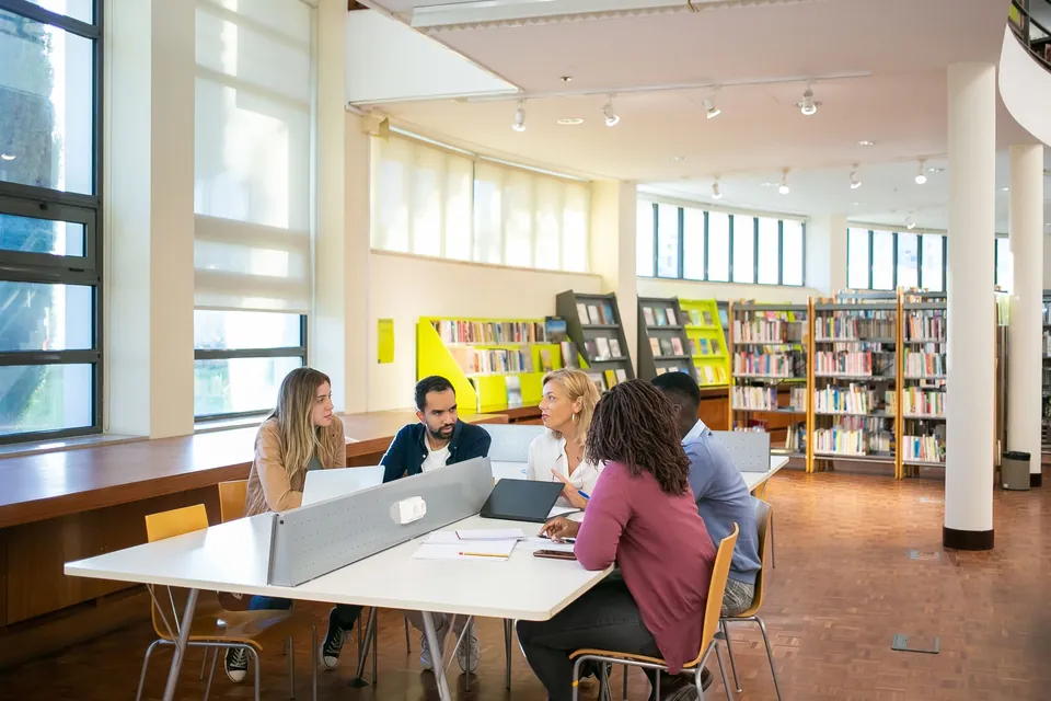 Students working at large tables in a bright library.