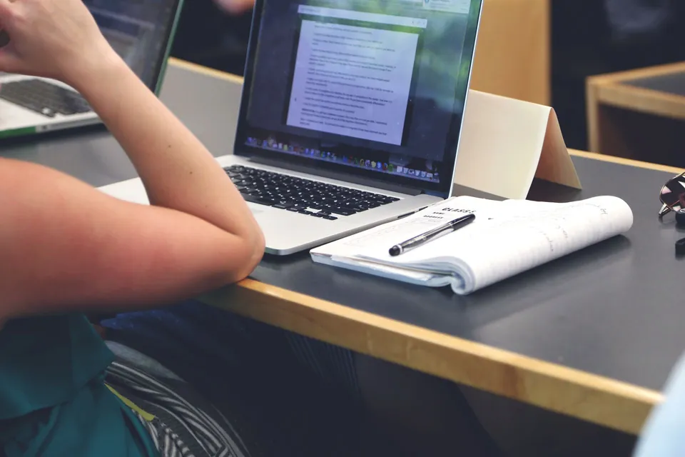 Person following a course on a laptop, with an open notebook beside it.