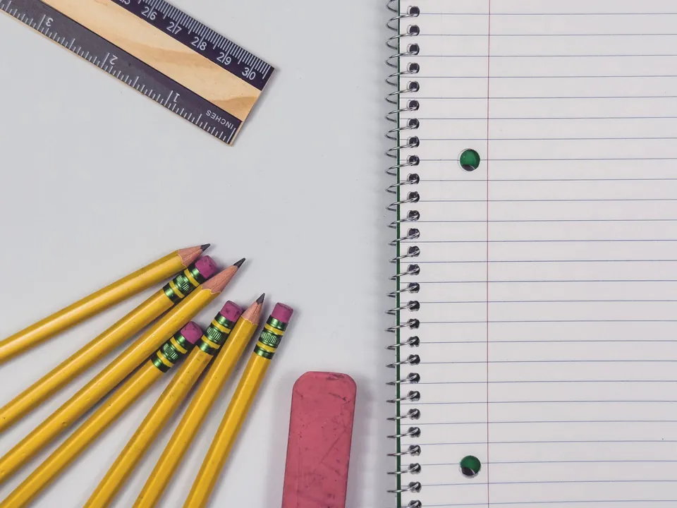 Pencils, an eraser, a ruler and a spiral notebook on a table.