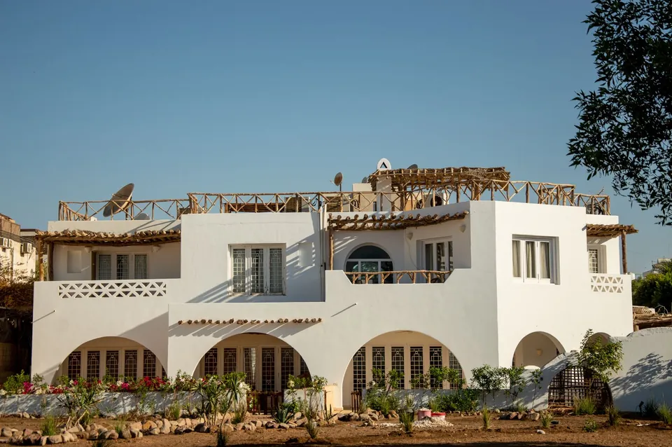 Large white house with arches and terraces under a blue sky.