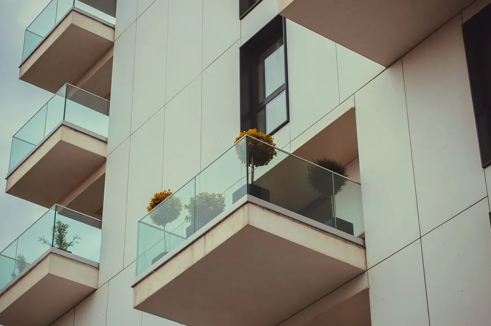 Recent apartment building facade with glass balconies and potted plants.