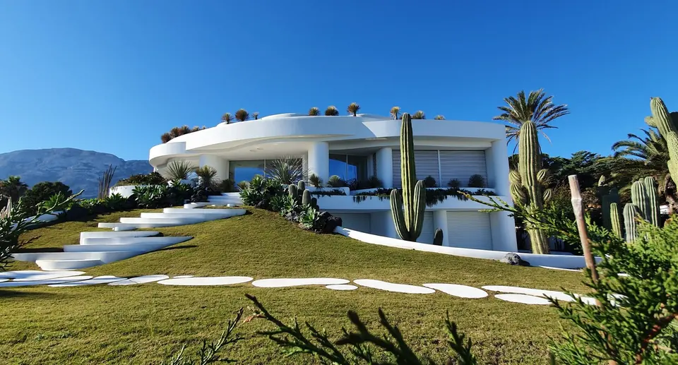 White villa with curved lines, surrounded by cacti and a lawn.