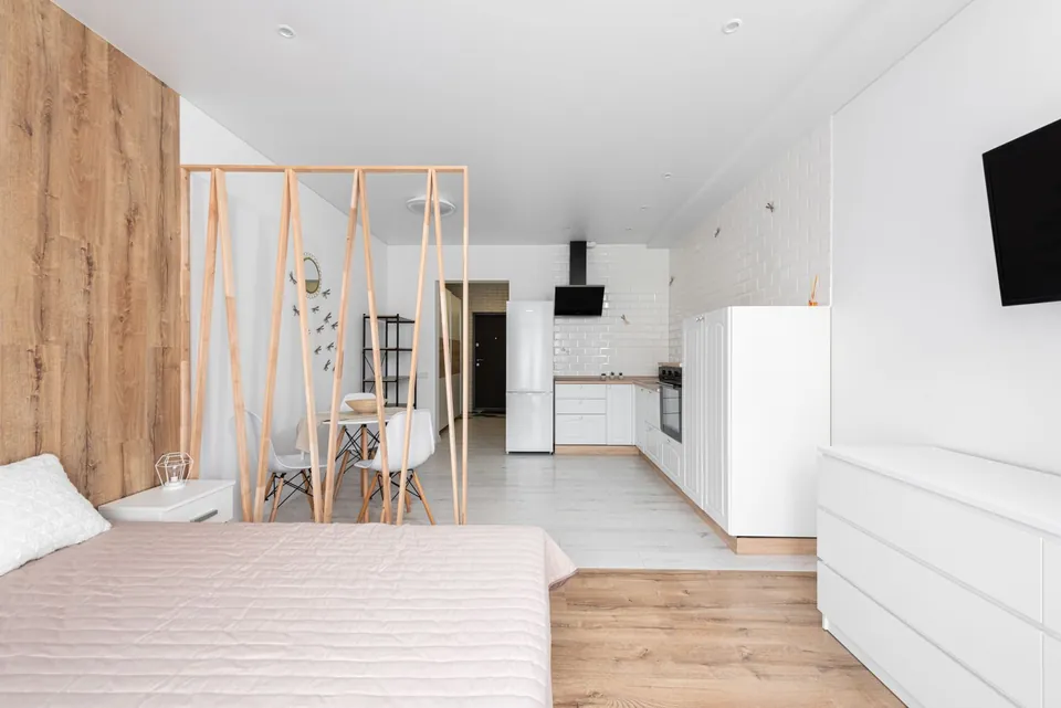 Furnished studio with a bed, a white kitchen and a light wood partition.