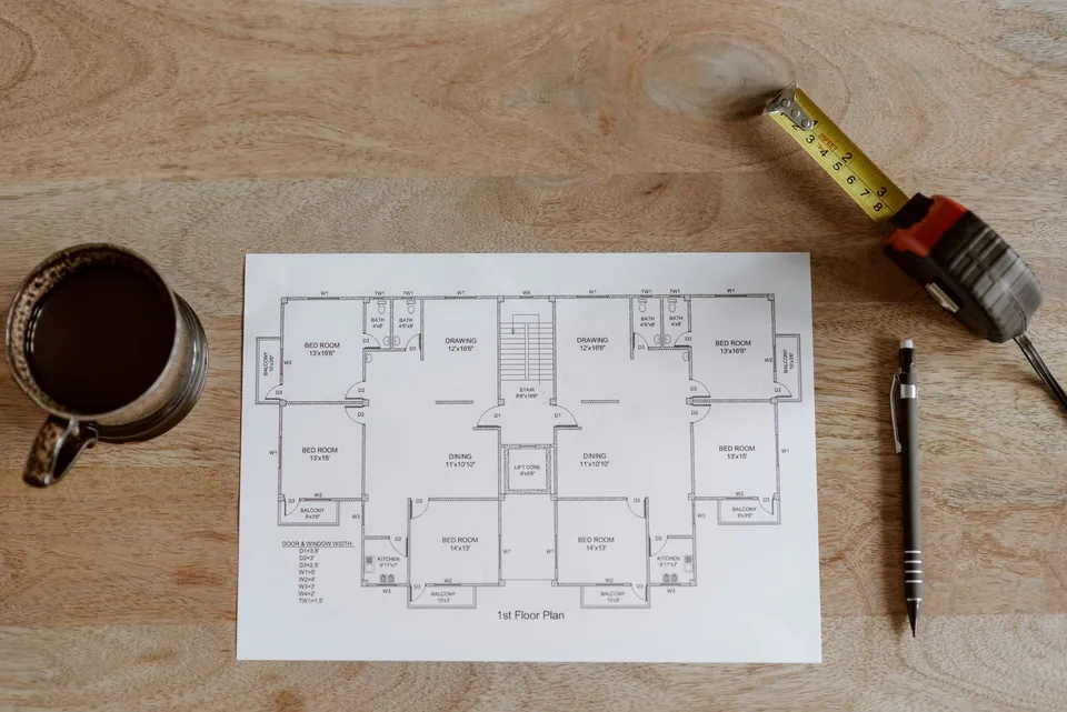 Floor plan, tape measure and pen on a wooden table.