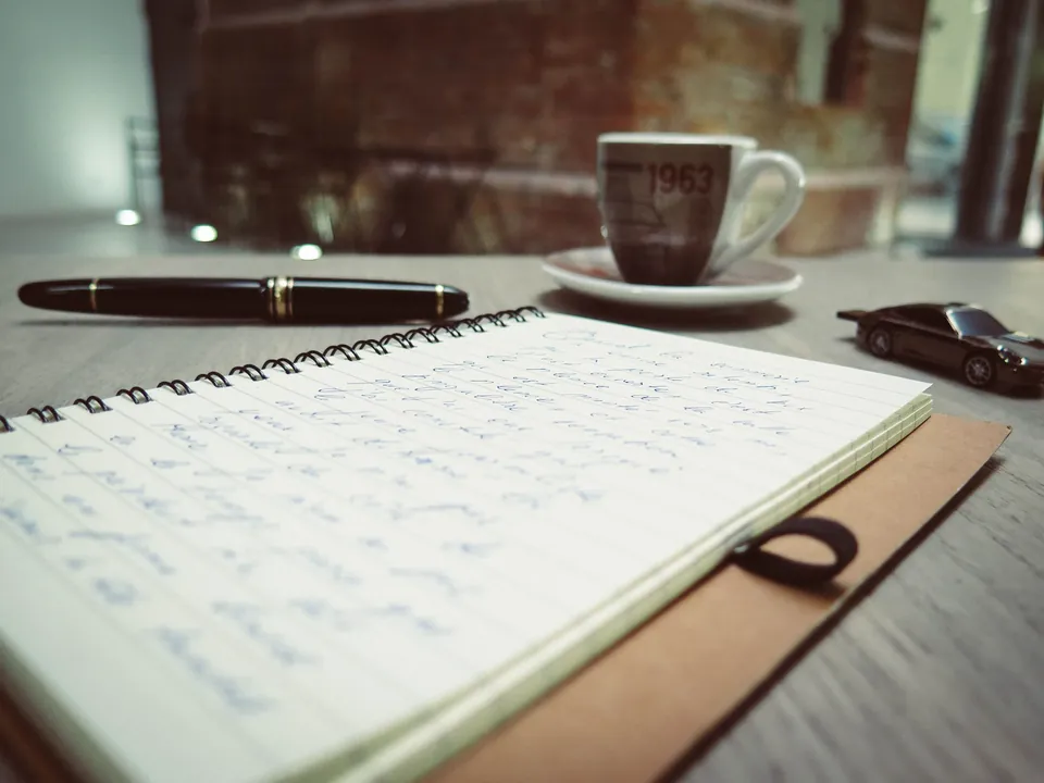 Notebook with handwritten notes, fountain pen and coffee cup on a table.