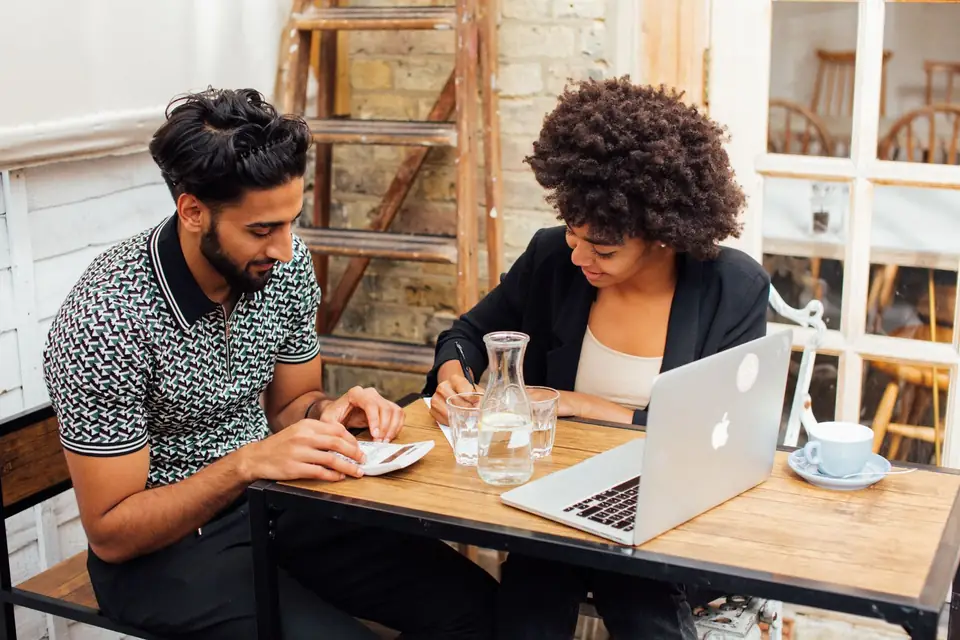 Two people talking over a laptop in a café.