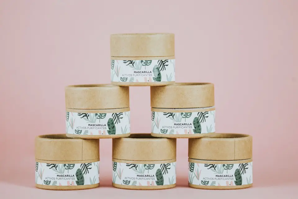 Labelled kraft cardboard jars stacked on a pink background.