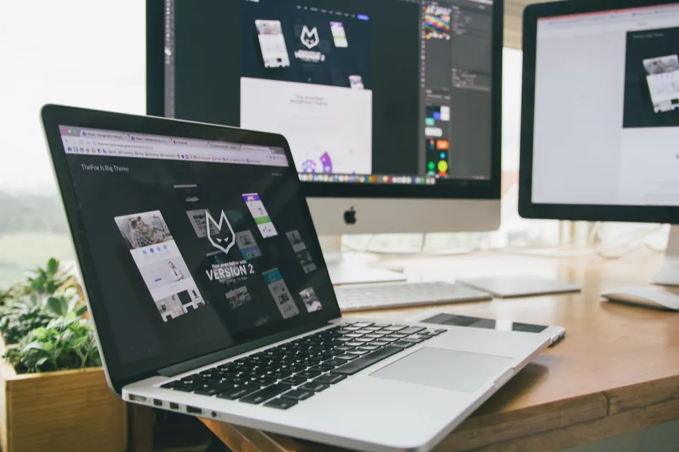 Laptop showing website mock-ups, work screens in the background.