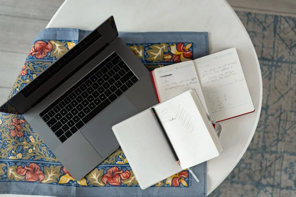 Laptop and open notebooks on a round table, seen from above.