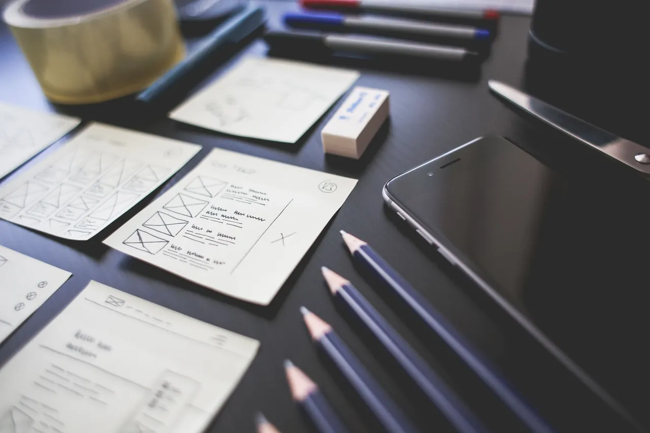 Paper sketches of app screens, pencils and a phone on a dark desk.