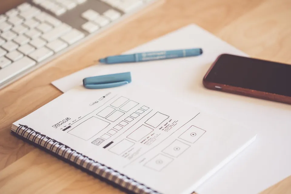 Spiral notebook with a sketched web page layout, a pen and a phone.