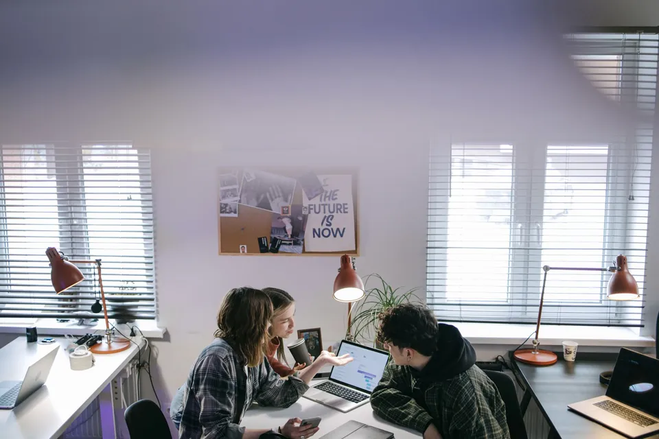 Three colleagues talking around a laptop in a bright office.